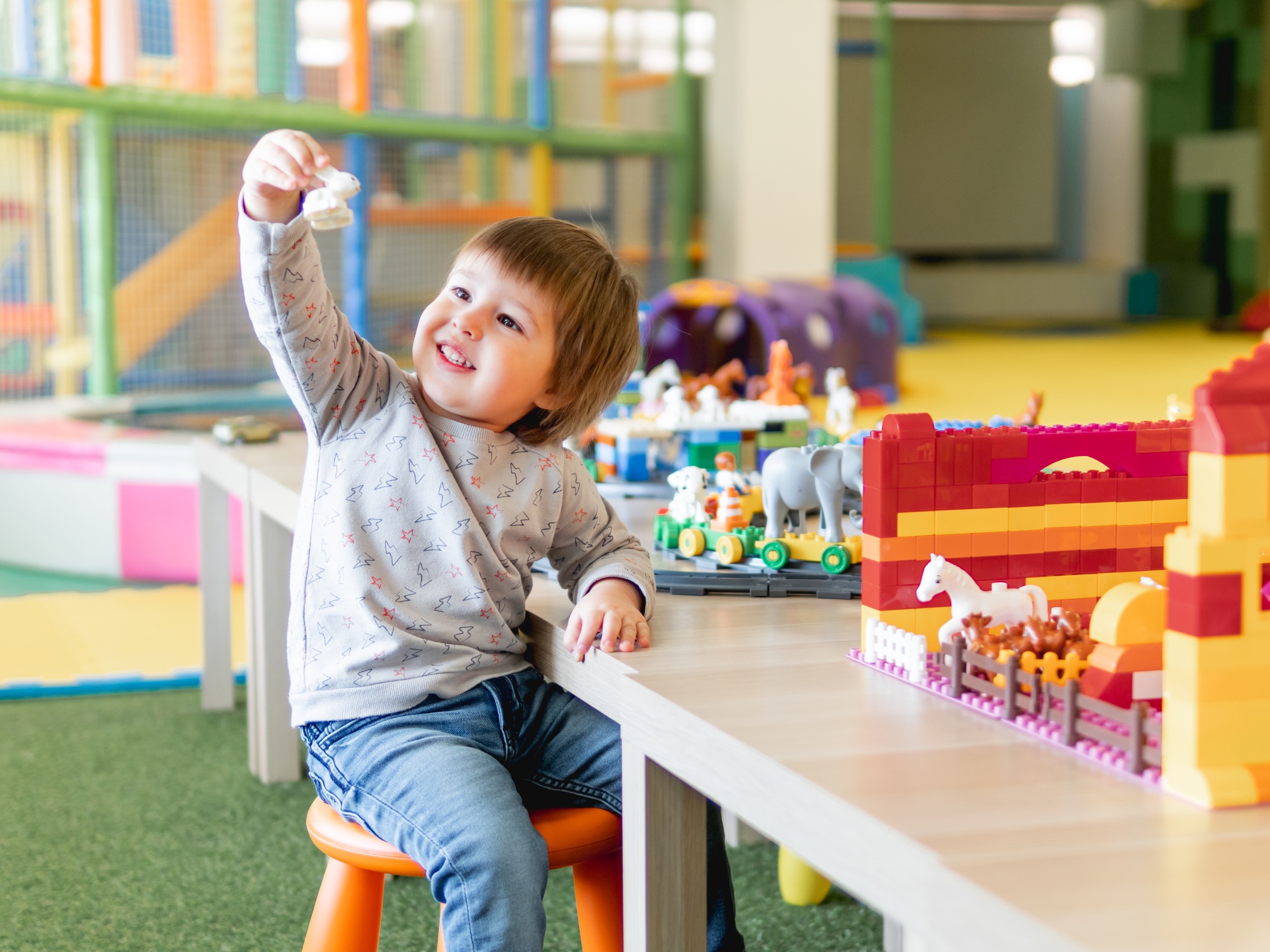 Toddler plays with toy constructor in nursery. Kid has fun in kindergarten.